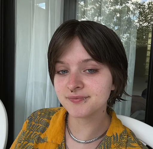 An image of a person with short brown hair and a smile, wearing a yellow fern-print shirt.